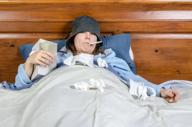 woman sick in bed with thermometer